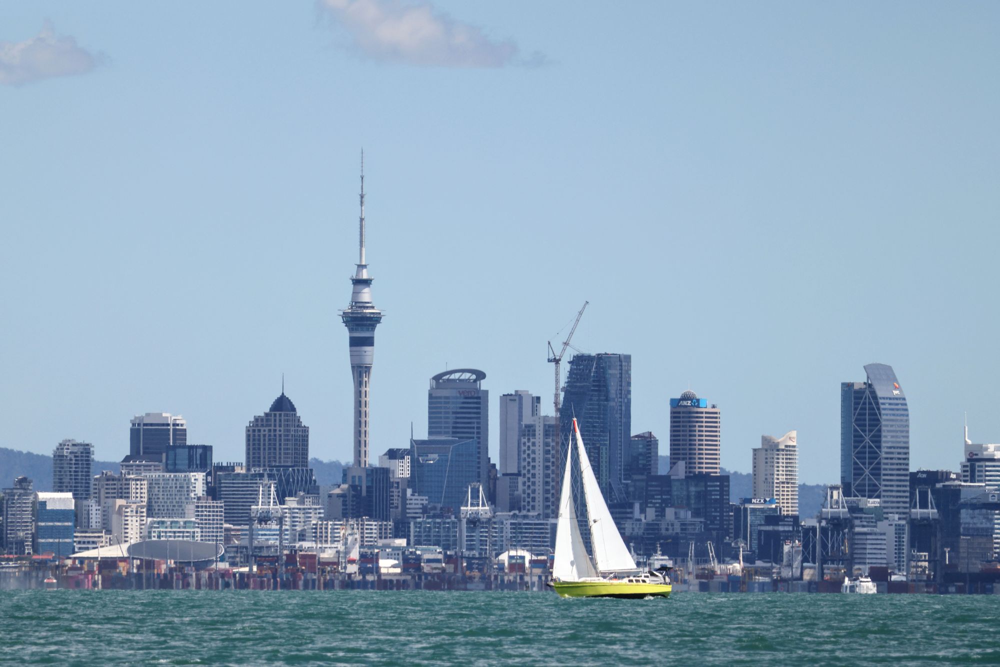 A yellow sailboat on the harbour in front of the Auckland skyline