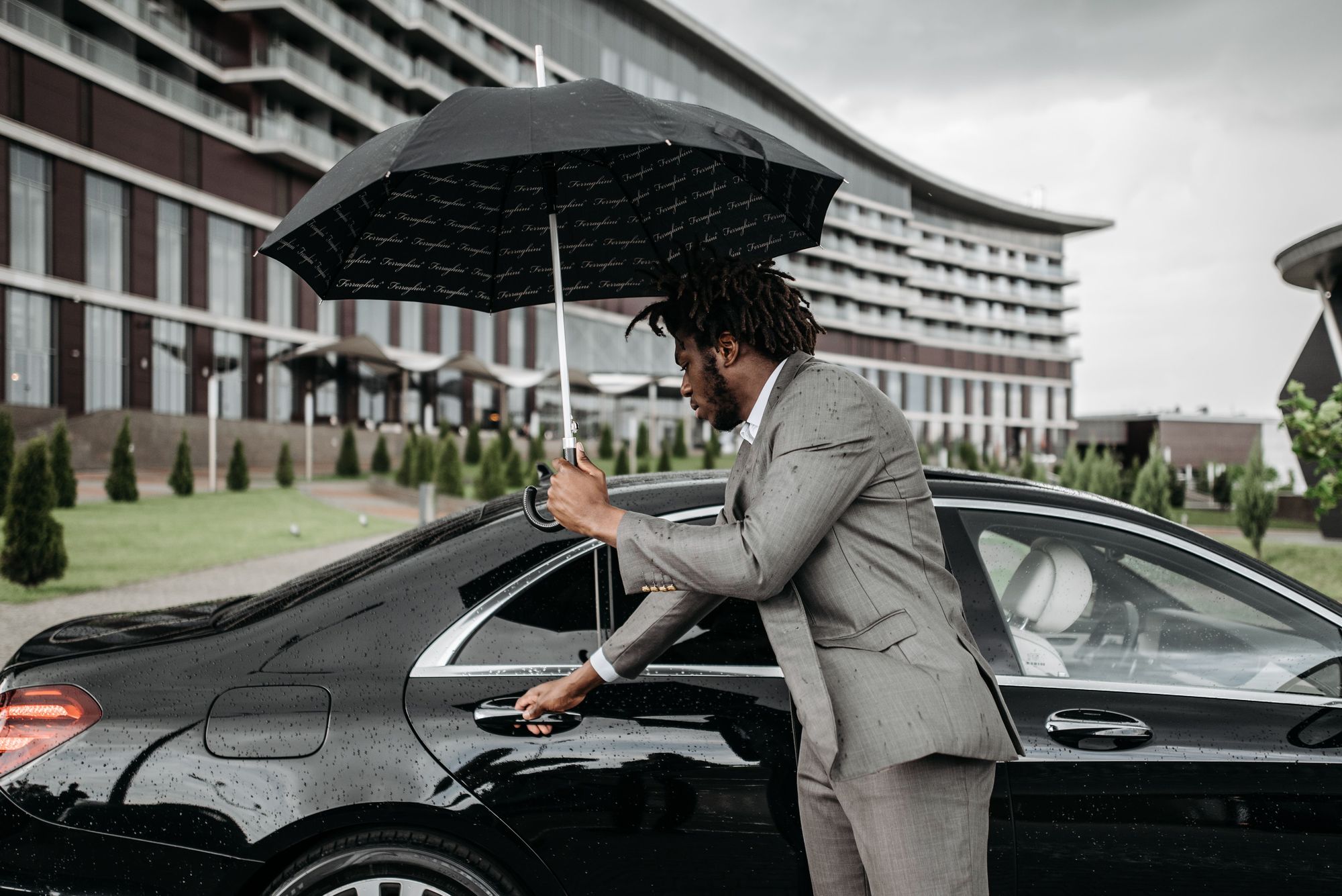 A chauffeur holding an umbrella beside a black car